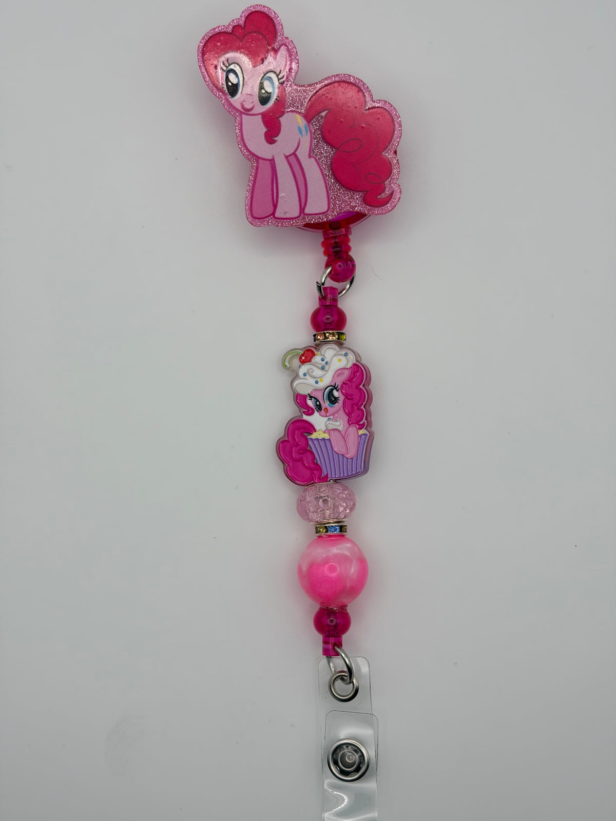Pink pony-themed badge reel with a sparkly border, pony-and-cupcake charm, pink beads, and clear snap badge strap.