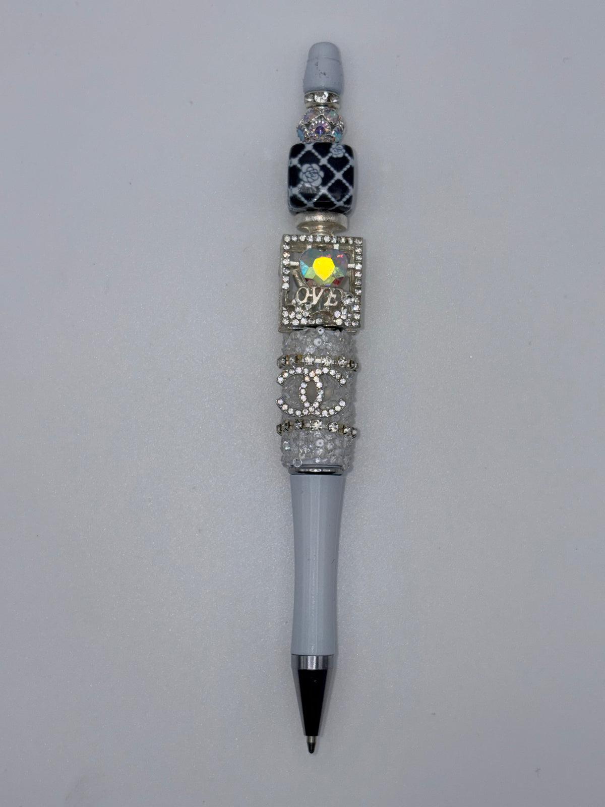 Gray beaded pen with black patterned bead, silver-tone sparkling accents, square LOVE decoration, and interlocking-letter detail on a plain background.