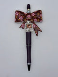 Dark plum pen with large brown bow patterned with pink flowers and gold-tone monogram motifs, sparkling LOVE accent, and silver-tone trim.