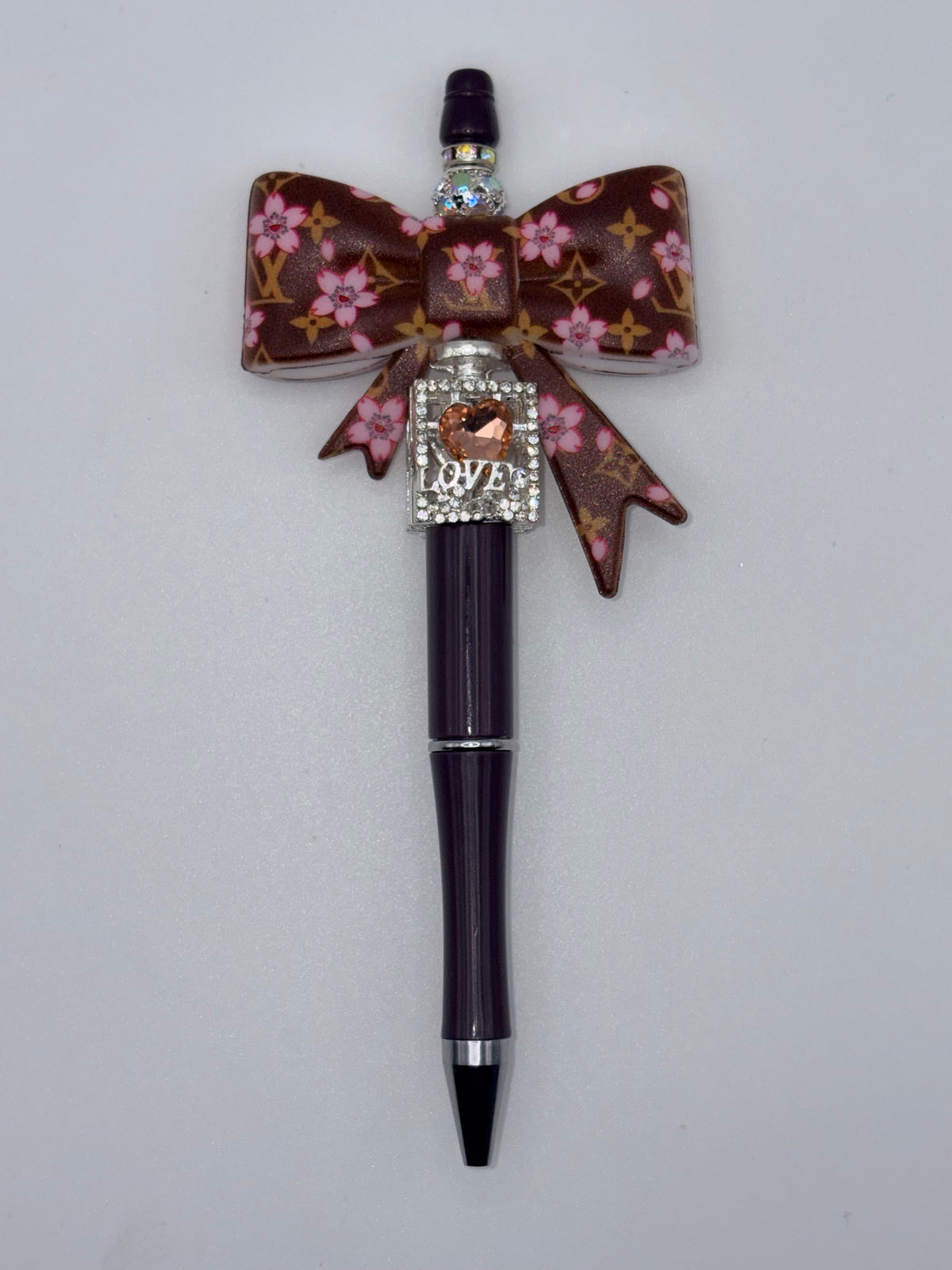 Dark plum pen with large brown bow patterned with pink flowers and gold-tone monogram motifs, sparkling LOVE accent, and silver-tone trim.