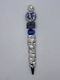 Blue and silver beaded pen with reflective heart-decorated barrel, deep blue bead, navy handbag-shaped accent, and round blue-and-white floral lettered accent.