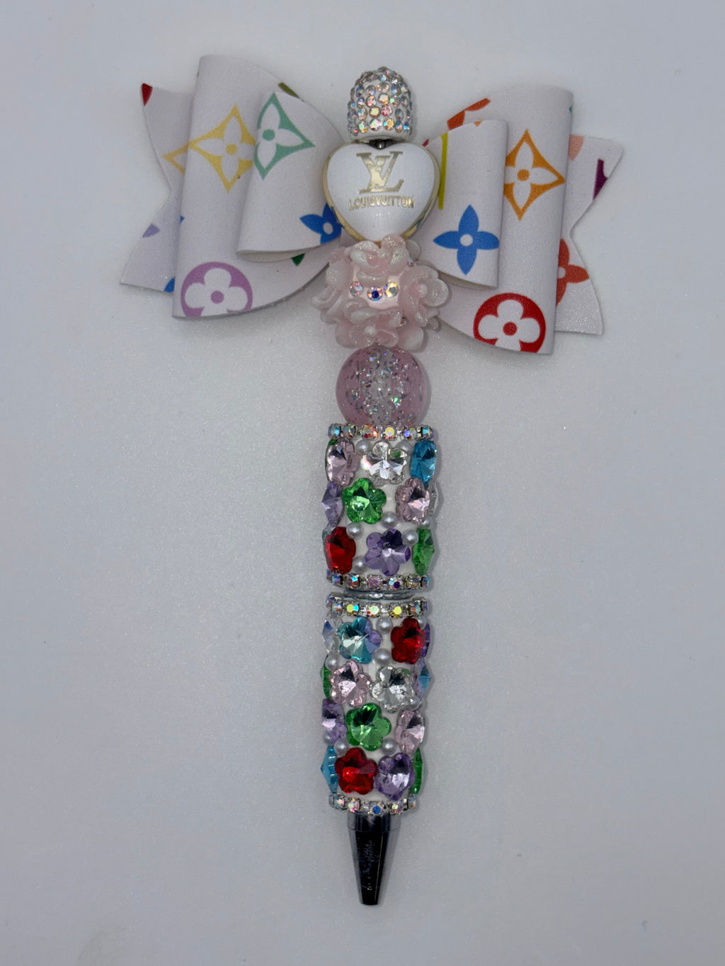 Beaded pen with white multicolor monogram-patterned bow, white heart accent, pale pink flower and glitter bead, multicolor sparkling barrel, and silver-tone tip.
