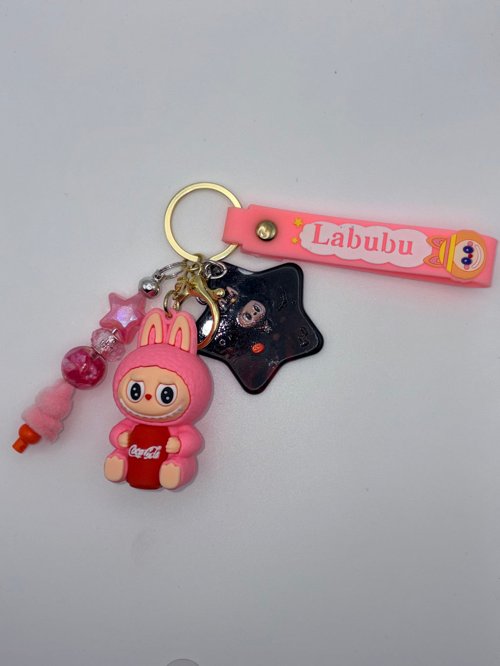 Pink Labubu-themed keychain with pink lettered strap, bunny-eared character holding a red soda can, black star charm, and pink beaded dangle.