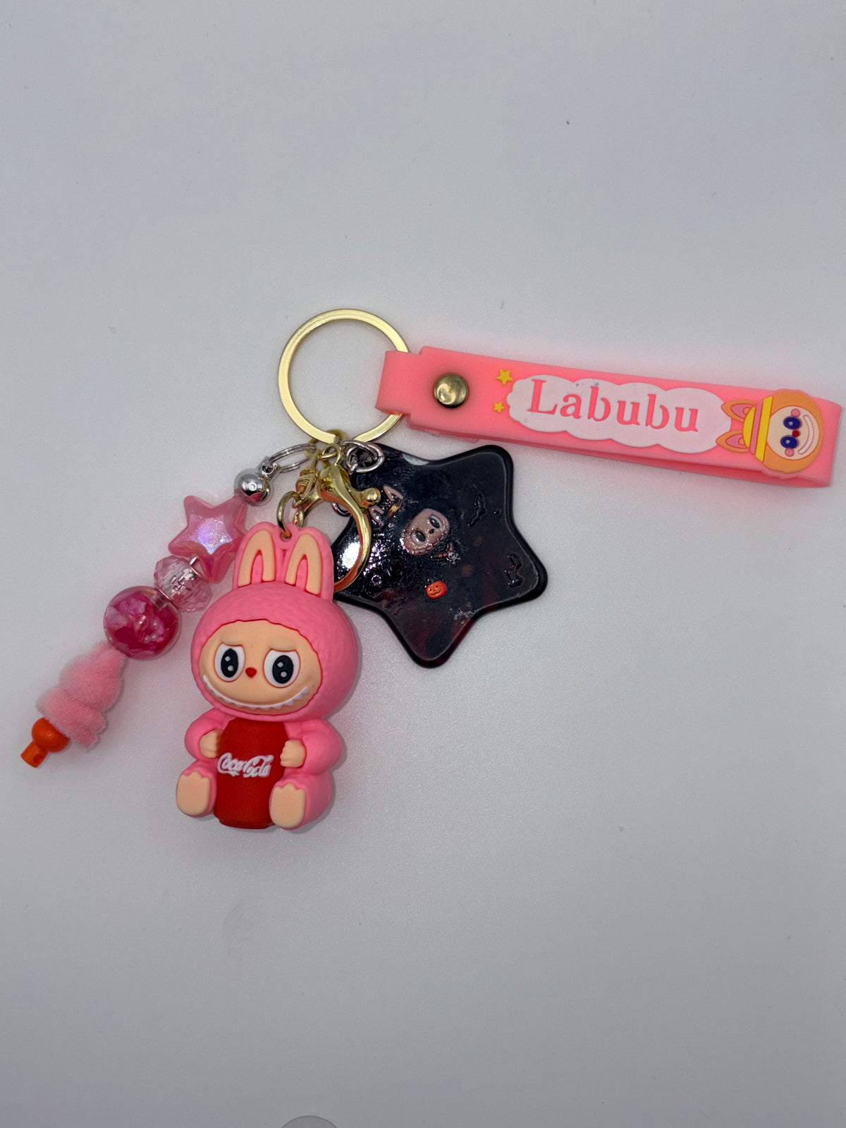 Pink Labubu-themed keychain with pink lettered strap, bunny-eared character holding a red soda can, black star charm, and pink beaded dangle.
