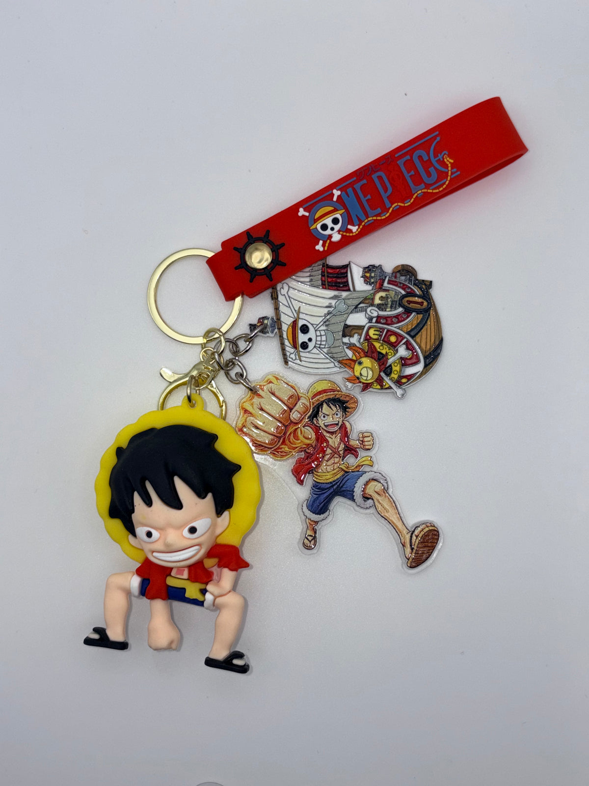 One Piece–themed keychain with a red wrist strap, dimensional Luffy charm, and flat Luffy and pirate-ship charms.