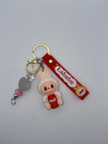Labubu-themed keychain with white bunny-eared character holding a red Coca-Cola cup, red Labubu strap, gold-tone key ring, and decorative beads.