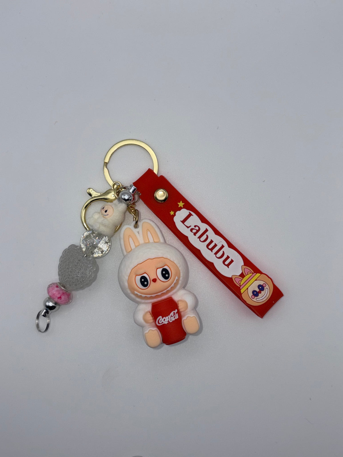 Labubu-themed keychain with white bunny-eared character holding a red Coca-Cola cup, red Labubu strap, gold-tone key ring, and decorative beads.