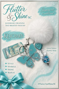 Aqua and white themed keychain with a butterfly charm bearing Tiffany & Co. lettering, white fluffy pom-pom, aqua heart accent, rectangular charm, and clear and aqua beads.